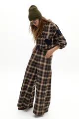 Pantalón de pierna ancha con estampado de cuadros en tonos beige, marrón y negro. Presenta tiro medio-alto, cierre frontal oculto y bolsillos laterales de apertura diagonal.