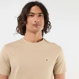 Remera lisa de manga corta en color beige, con cuello redondo y un pequeño bordado en el pecho que representa una taza de café.