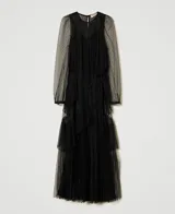 Vestido largo de tul negro con volantes plisados e inserciones de encaje. Presenta un escote redondo con lágrima, manga larga transparente, cremallera invisible lateral, cinturón fino de la misma tela y combinación, de corte ancho.