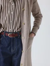 Cárdigan largo de tejido de punto, color beige topo, con mangas largas y botones frontales. Presenta un calce holgado y bolsillos delanteros.