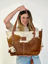 Bolso tipo tote Chabas modelo Molly, confeccionado en cuero con pelo natural en tonos marrón y blanco. Posee asas largas de cuero marrón, parche frontal con la marca grabada y un charm colgante decorativo en forma de estrella con detalle de pelo.