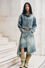 Falda midi de denim con lavado claro, tiro medio y cintura cruzada con cierre asimétrico de cremallera y botones metálicos. Presenta bolsillos delanteros y bajo asimétrico.