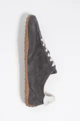 Zapatillas deportivas de perfil bajo confeccionadas en serraje color gris, con cordones claros y suela de goma con tachuelas características.