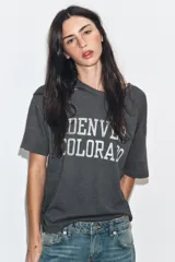 Camiseta de corte oversize confeccionada en algodón flamé, con cuello redondo y manga corta. Presenta un diseño con efecto desgastado, detalles de roturas en el tejido y estampado de texto a contraste en la parte frontal.