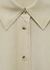Camisa color beige de corte crop, confeccionada en mezcla de lino y lyocell. Tiene cuello camisero, mangas largas con puños abotonados, lazo ajustable en la cintura y cierre frontal con botones.