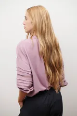 Camisa de color crudo con diseño romántico, cuello redondo con cordón ajustable terminado en borlas, y mangas tres cuartos abullonadas. Presenta detalles de bordados calados verticales en el frente y horizontales en las mangas.