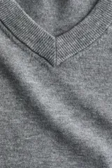Buzo de punto fino color gris melange, con escote en V y remate acanalado ancho en puños y bajo.