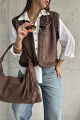 Chaleco de gamuza color chocolate con interior y bordes de corderito sintético. Presenta diseño con tachas metálicas decorativas en el frente y los hombros.