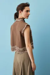 Camisa cropped sin mangas color tostado, con cuello clásico, cierre frontal de botones, bordado calado y terminación festoneada en el ruedo.