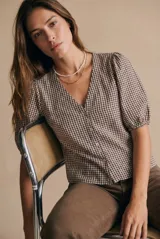 Blusa de algodón con estampado de cuadros vichy en tonos negro y blanco. Presenta escote en V, cierre frontal con botones y mangas cortas abullonadas con terminación elástica.