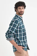 Camisa de manga larga con estampado de cuadros en tonos verde petróleo, blanco y líneas finas en color ocre. Presenta cuello clásico con botones y puños con detalle en contraste.