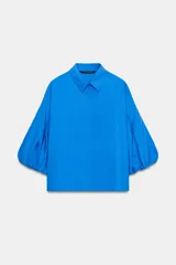 Camisa roja de cuello solapa, con mangas cortas abullonadas tipo globo y cierre frontal con botones ocultos.