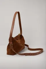 Cartera mediana de gamuza color tostado con detalles en cuero liso al tono. Cuenta con doble asa fija para llevar al hombro y una correa larga desmontable y regulable para usar como bandolera. Posee cierre superior.