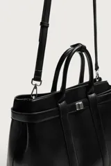 Bolso de mano estructurado en color negro, con diseño minimalista y detalle de cinturón decorativo en la parte superior. Cuenta con doble asa de mano y cierre magnético.