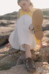 Sandalias de cuero marrón con diseño de tiras entretejidas y hebilla lateral.