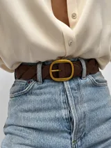 Cinto trenzado de símil cuero color marrón, con hebilla rectangular metálica en tono dorado.