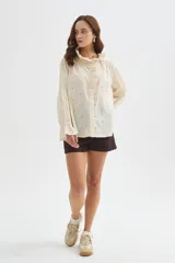 Camisa de algodón con detalles de broderie, volados y cuello a la base. Presenta diseño holgado, cierre frontal con botones y mangas largas con puños fruncidos.