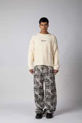 Sweater de punto acanalado con diseño de calce relajado, cuello redondo y mangas largas. Presenta una estampa gráfica pequeña en el centro del pecho y un parche con logo en el puño.