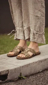 Sandalias planas de cuero negro, con diseño de tiras anchas interconectadas y punta cuadrada, decoradas con tachas metálicas doradas.