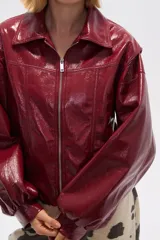 Chaqueta corta de cuero sintético negro con cuello camisero, cierre frontal con cremallera, bolsillos laterales y mangas largas abullonadas.