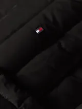 Campera negra acolchada de nylon con relleno de plumas, cuello redondo, cierre con botones a presión, bolsillos laterales con botones a presión y logo de Tommy Hilfiger bordado en el pecho.