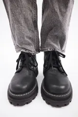 Borcego de cuero color gris con cordones color naranja, suela track negra de goma y detalle de gamuza en la parte superior del tobillo.