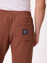 Pantalón tipo babucha de algodón y poliéster en color marrón, con cintura elástica, bolsillos laterales y logo de la marca bordado en la pierna izquierda.