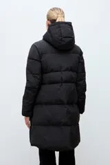 Campera puffer larga de color negro, con diseño capitoneado, capucha integrada y cierre frontal oculto. Presenta cierres laterales en el ruedo para mayor comodidad.