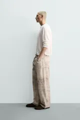 Pantalón de corte baggy fit confeccionado en tejido de algodón con efecto lavado y estampado abstracto en tonos beige y gris. Presenta diseño de cinco bolsillos, cierre frontal con cremallera y botón.