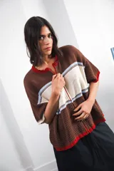 Remera de punto con diseño retro de bloques de color en marrón, crema y celeste. Presenta cierre frontal, cuello redondo, mangas cortas y tejido calado en la parte inferior. Incluye detalle de logo en relieve en el frente.