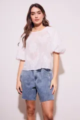 Blusa blanca traslúcida con estampado floral en relieve, cuello redondo y mangas globo cortas.