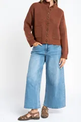 Cardigan de lana color marrón, con cuello alto, cierre frontal de botones y dos bolsillos delanteros. Presenta puños y ruedo acanalados.