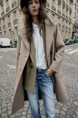 Abrigo largo cruzado color gris oscuro, confeccionado con lana. Presenta cuello solapa, manga larga, bolsillos delanteros de plastrón y cierre frontal con botones.