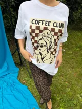 Remera oversize de algodón negro, con diseño gráfico frontal que incluye la leyenda "COFFEE CLUB" y una ilustración estilo retro de una mujer bebiendo café.