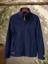 Campera de polar azul marino con cierre frontal completo, cuello alto, bolsillos laterales y un bolsillo vertical en el pecho. Presenta detalles en cuero sintético en el tirador del cierre y una etiqueta de marca en el ruedo.