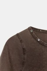 Camiseta de cuello redondo y manga corta con efecto lavado. Presenta detalle de tachas metálicas en el escote y bajo asimétrico.