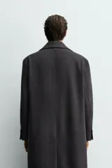 Abrigo de corte relajado con diseño de cuadros sutiles, cuello con solapas de muesca y cierre frontal de botonadura cruzada. Cuenta con mangas largas con puños abotonados, bolsillos laterales con solapa y abertura central en la espalda.