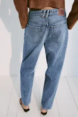 Jeans mom fit de tiro alto confeccionados en denim azul claro, con diseño de cinco bolsillos, trabillas para cinturón y cierre frontal con cremallera y botón metálico.