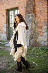 Ruana de tejido liviano color beige, con diseño abierto y detalles de volados en mezcla de lino y algodón. Presenta terminaciones con flecos en el ruedo y cordones decorativos con borlas en el frente.