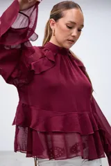 Blusa color bordó con cuello alto, mangas largas acampanadas y detalles de volados en el pecho y el ruedo.