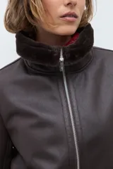 Chaqueta de eco cuero color chocolate con interior y cuello forrados en piel sintética al tono. Presenta cierre frontal completo, bolsillos laterales y diseño de corte recto.