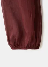 Vestido largo de tejido fluido color bordó, de diseño evasé con escote en pico y mangas largas con puños elásticos. Presenta detalles de volantes en el cuello y forro interior.