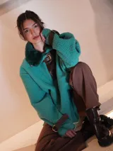 Buzo verde agua con cuello y solapa de cuero marrón. Presenta cierre frontal con hebilla y puños con correa ajustable.