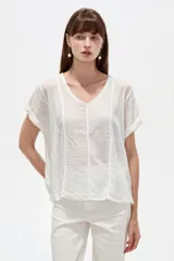 Blusa de algodón blanca de corte holgado, con cuello redondo y detalles de broderie en las mangas y costuras frontales.