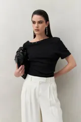 Top tejido color crudo, de silueta ajustada con diseño minimalista y escote redondo, adornado con pequeños botones metálicos.