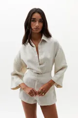 Short de lino color natural, de cintura alta con elástico en la parte trasera, ruedo curvo, bolsillos laterales y cierre frontal escondido.