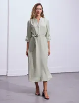 Vestido maxi color beige, con cuello mao y escote en V. Presenta mangas largas con presilla y botón para regular el largo, y un lazo ajustable en la cintura que marca la silueta.