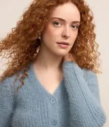 Cardigan cropped de punto color rosa claro, con textura de pelito, cuello en V, mangas largas, cierre frontal con botones y bolsillos delanteros.