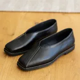 Zapato bajo de cuero negro con punta cuadrada y detalle de cierre en la capellada.