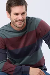 Remera de manga larga con diseño de rayas horizontales anchas en tonos verde, bordó y azul marino. Presenta cuello redondo y una pequeña estampa tipográfica en el pecho.